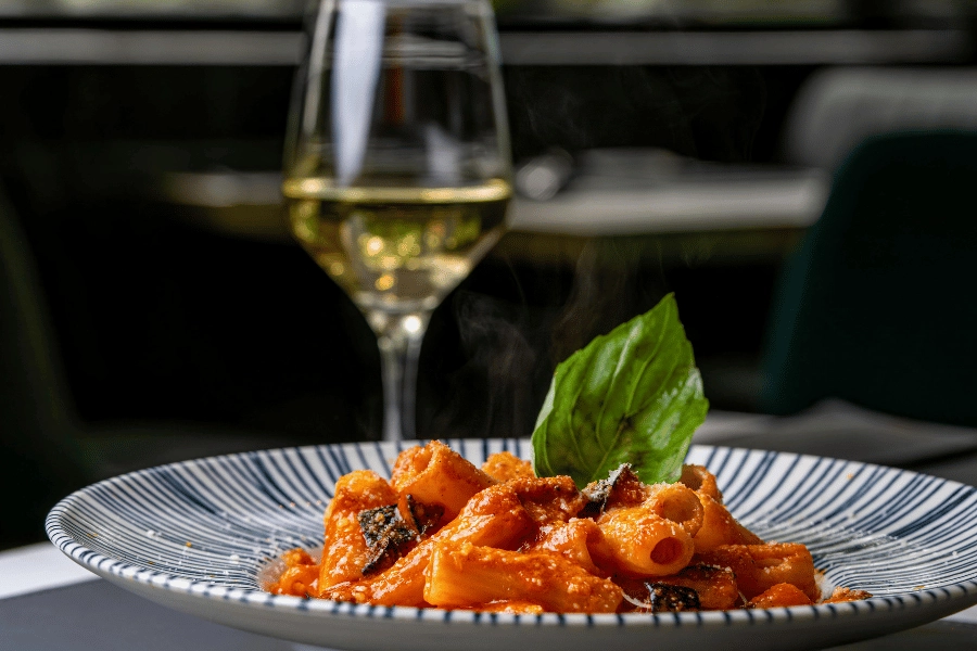 plate of delicious pasta in a red sauce alongside a glass of white wine